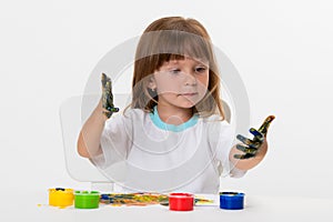 Close-up portrait of a cute cheerful happy smiling little girl draws her own hands with gouache or finger paints isolated on white