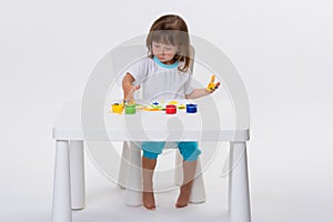 Close-up portrait of a cute cheerful little girl draws her own hands with gouache or finger paints at the table isolated on white