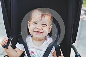 close-up portrait of a cute girl 9 months old, who sits in a black stroller on the street and makes a funny face