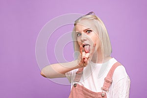 Close-up portrait of a cute girl in a bright casual clothing shows a sign of heavy metal and makes a serious face on a blue