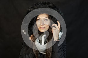 Close-up portrait of beautiful girl with jacket and fur hood on dark background