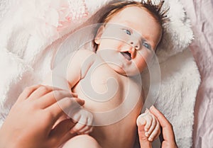 Close-up portrait of cute happy smiling baby girl lying down on bed. Mother is holding her newborn baby. Small daughter