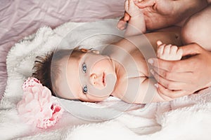 Close-up portrait of cute happy smiling baby girl lying down on bed. Mother is holding her newborn baby. Small daughter