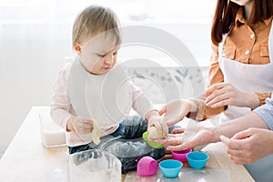 Close-up portrait of cute little baby girl sitting on the dinner table and playing with dough for baking muffins in