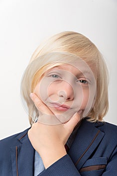 Close up portrait of a cute little boy with blond hair in a suit holding his chin