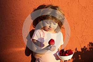 Close up portrait cute little boy holding a strawberry. Lovely child eating strawberries.