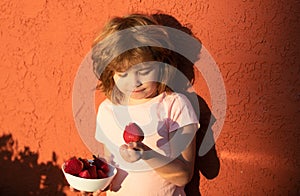 Close up portrait cute little boy holding a strawberry. Lovely child eating strawberries.