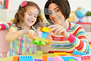 Close up portrait of cute little girl and her mother playing colorful plastic blocks together in her room