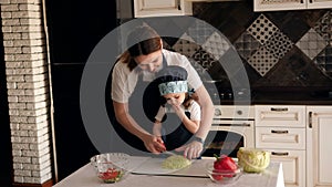 Close-up portrait of a cute little girl in the kitchen, she eats fresh cabbage.