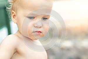 Close-up portrait of cute pensive upset caucasian 2 year old toddler boy portrait standing alone at beach summer day and