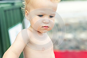 Close-up portrait of cute pensive upset caucasian 2 year old toddler boy portrait standing alone at beach summer day and looking