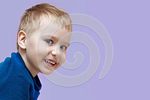 Close up portrait of cute smiling sly baby boy in blue sweater isolated on pink background, looking right into the camera.