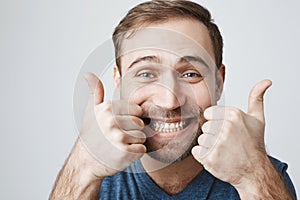 Close-up portrait of dark-haired bearded male customer with broad smile, demonstrating white teeth, looking at the