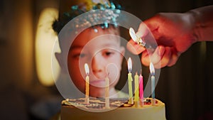 Close-up portrait in defocus of a little boy sitting at a table, mother to her son on his birthday lights candles on a