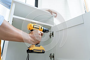 Close up portrait and details of caucasian male worker using electric screwdriver instrument in hand and repairing new wooden desk