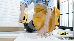 Close up portrait and details of caucasian male worker using electric screwdriver instrument in hand and repairing new wooden desk