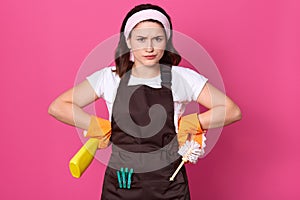 Close up portrait of dissatisfied young dark haired lady with angry facial expression, wearing headband, rubber gloves and brown