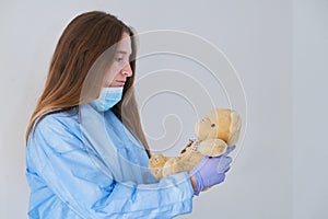 A close-up portrait of a doctor wearing an operating theatre outfit and brazing a teddy bear - isolated on a blue background.