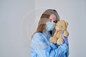 A close-up portrait of a doctor wearing an operating theatre outfit and brazing a teddy bear - isolated on a blue background.