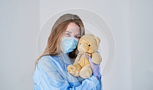 A close-up portrait of a doctor wearing an operating theatre outfit and brazing a teddy bear - isolated on a blue background.