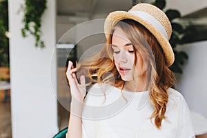 Close-up portrait of dreamy young lady with curly hairstyle and pale skin wearing elegant straw hat decorated with white