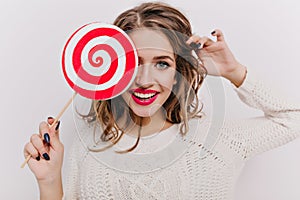 Close-up portrait of ecstatic young female model with bright makeup posing with sugar-candy in studio. Enthusiastic girl