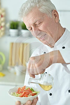 Close-up portrait of elderly male chef pouring oil into salad