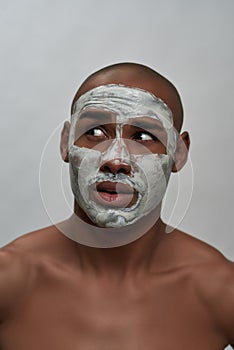 Close up portrait of emotional young african american man looking aside, using facial clay mask, posing isolated over