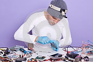 Close up portrait of engineer repairs phone, master opening back cover of phone, radioman sitting at table surrounded with