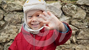 close-up Portrait of European little preschool boy in gray knitted hat red jacket smiling look at camera. Emotionally