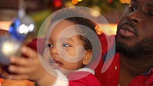 Close-up portrait of excited African American toddler son playing with New Year toy on Christmas tree as happy young