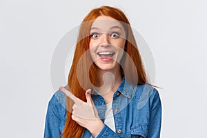 Close-up portrait excited happy ginger girl, foxy hair and blue eyes, smiling upbeat with amazement and joy, pointing