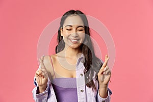 Close-up portrait of excited, optimistic and hopeful pretty girl in stylish outfit, cross fingers close eyes and smile