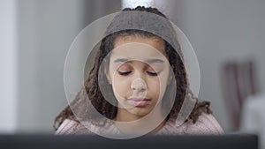 Close-up portrait of exhausted teenage African American student rubbing tired eyes sitting in front of laptop at home