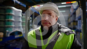 Close-up portrait of experienced Caucasian male forklift driver in hard hat sitting in vehicle looking around at stock