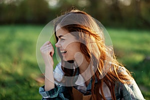 Close-up portrait of the face of a smiling, beautiful redheaded young woman in nature in a green park at sunset