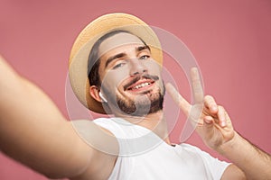Close up portrait of fashion handsome bearded young hipster blogger in white shirt and casual hat posing and making selfie on