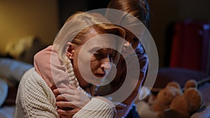 Close-up portrait of fatigue Ukrainian mother hugging frightened daughter with red air raid alert lamp flashing at