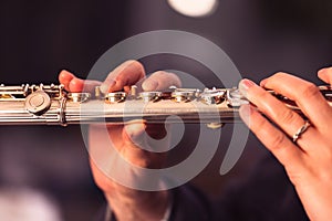 A close up portrait of the fingers of a hand of a flutist musician gripping down on the valves of a silver metal flute to play a