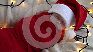 Close Up Portrait First Days Of Life Newborn Cute Funny Sleeping Baby In Santa Hat Wrapped In Red Diaper At White