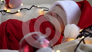Close Up Portrait First Days Of Life Newborn Cute Funny Sleeping Baby In Santa Hat Wrapped In Red Diaper At White