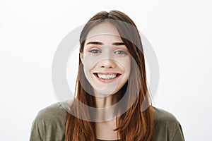 Close-up portrait of friendly charming european brunette with broad positive smile, standing over gray background