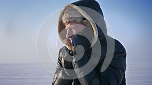 Close-up portrait of frozen businessman in hood talking busily on cellphone in snow desert.