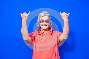 Close up and portrait of funny and crazy senior or mature woman doing surfing sign and smililing looking at the camera with blue