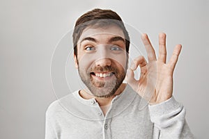 Close-up portrait of funny european guy showing okay or fine sign while smiling with excitement, being upbeat having