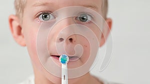 Close up Portrait funny face kid with electric toothbrush. child boy brushing teeth on white brick background. Health