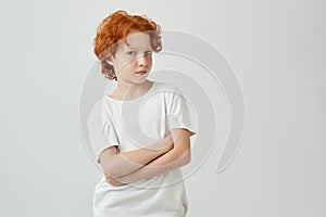 Close up portrait of funny ginger boy with freckles in white t-shirt looking in camera with relaxed expression and