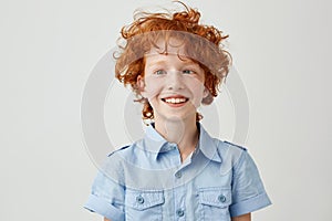 Close up portrait of funny little boy with orange hair and freckles mowing eyes, smiling and making silly faces for