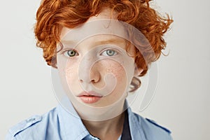 Close up portrait of funny little kid with orange hair and freckles. Boy looking in camera with relaxed and calm face