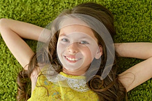 Close-up portrait of funny smiling little girl lying on green carpet